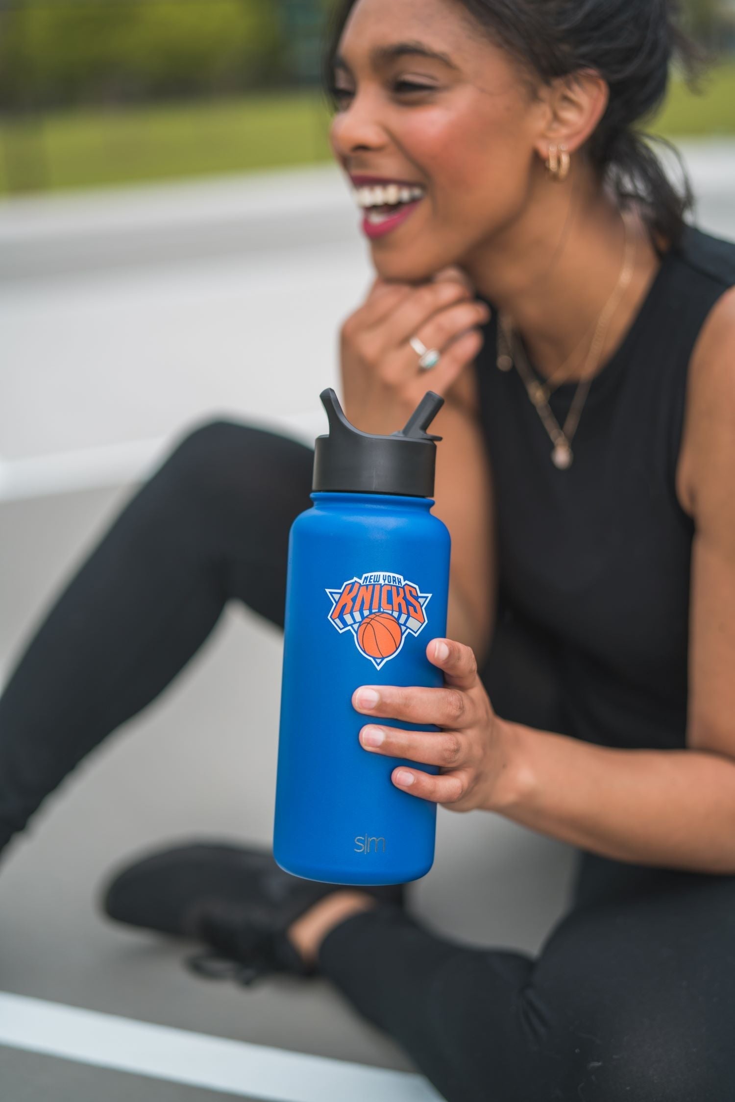 Person holding a vibrant royal blue water bottle, wearing black clothing against a neutral background