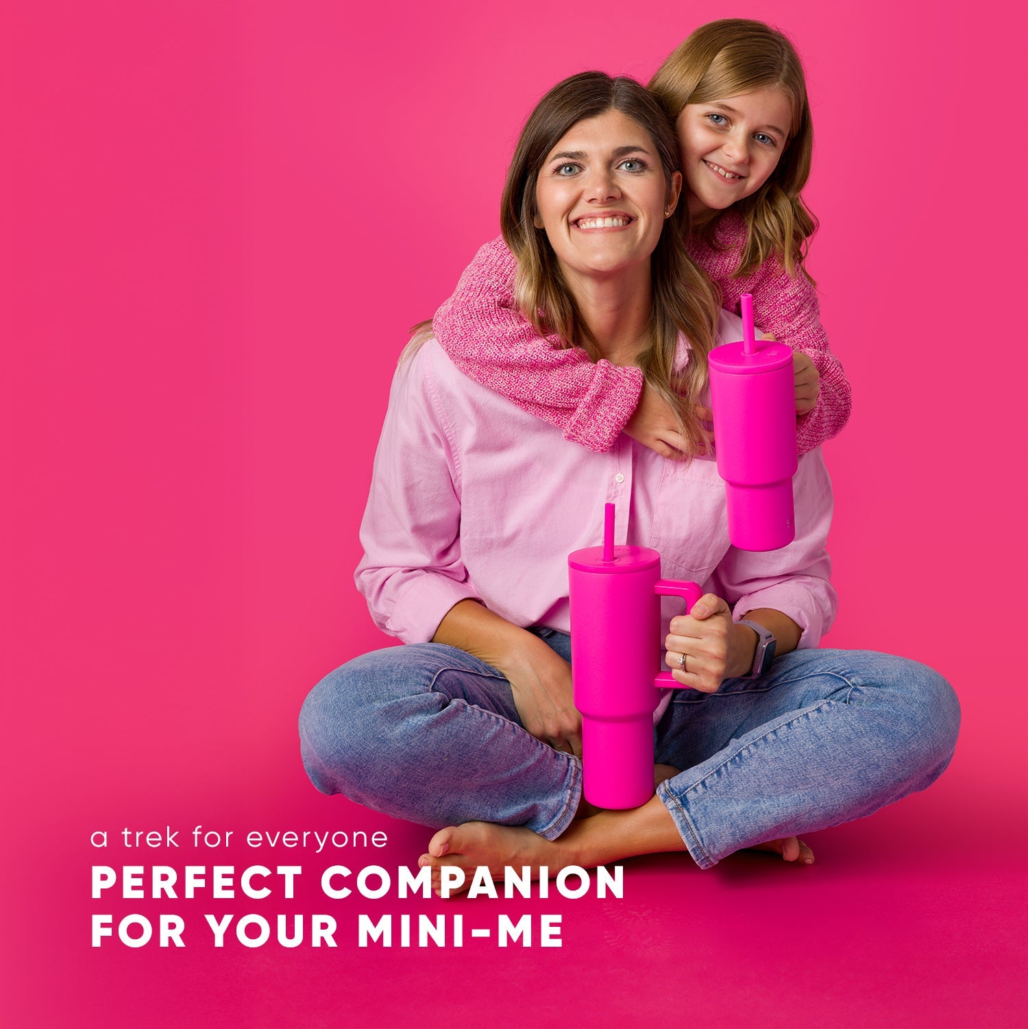 Adult woman and child smiling together against hot pink background, both holding matching Simple Modern 24oz hot pink Trek tumblers with straws. Both wear blue jeans and pink scarves. Text reads "Perfect companion for your