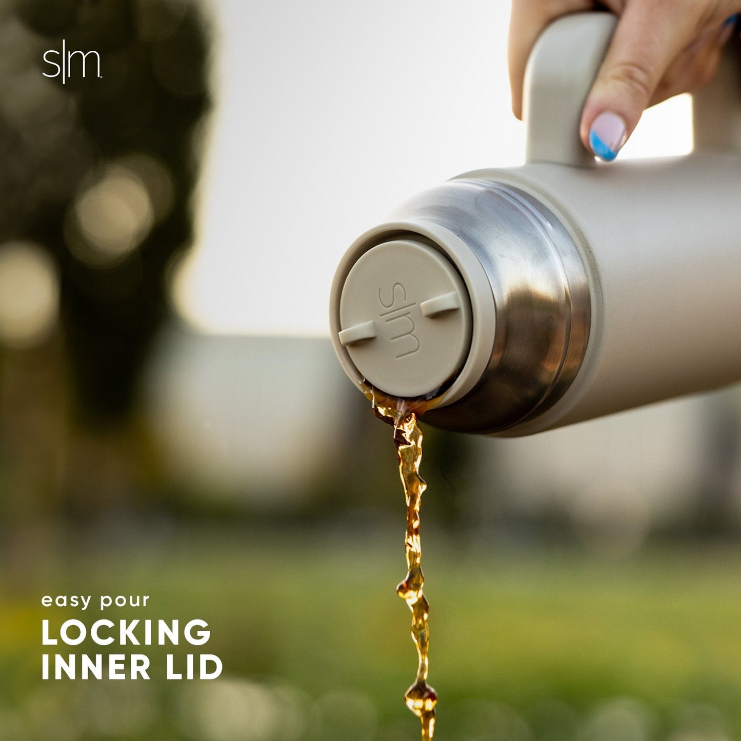 Stainless steel water bottle with locking inner lid pouring golden amber water against neutral cream and gray background